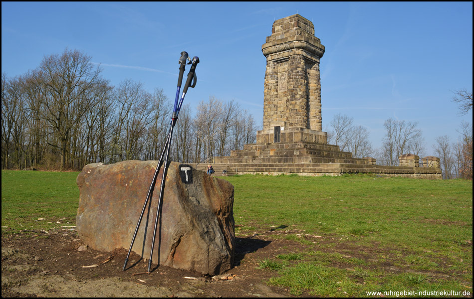 Wanderstöcke lehnen an Stein mit Wanderzeichen des 3 TürmeWEG Hagen vor dem Bismarckturm