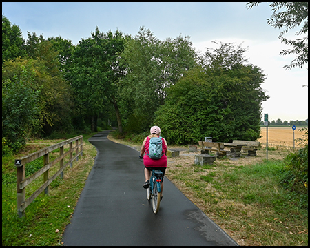 Radfahrerin auf einem Radweg passiert einen Rastplatz mit Tisch und Sitzbänken