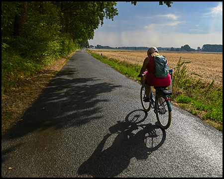 Radfahrerin auf einer schmalen Straße am Rande von Feldern fährt auf schlechtes Wetter zu