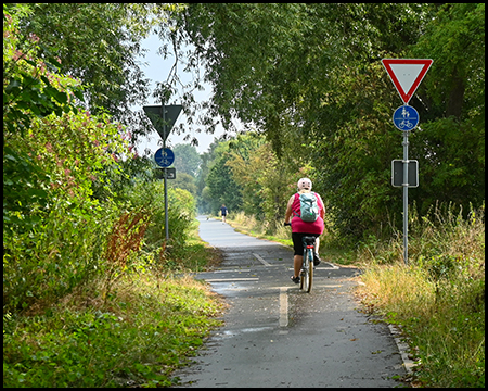Eine Radfahrerin auf einem schmalen Radweg vor einer Kreuzung mit Vorfahrt-Gewähren-Schild