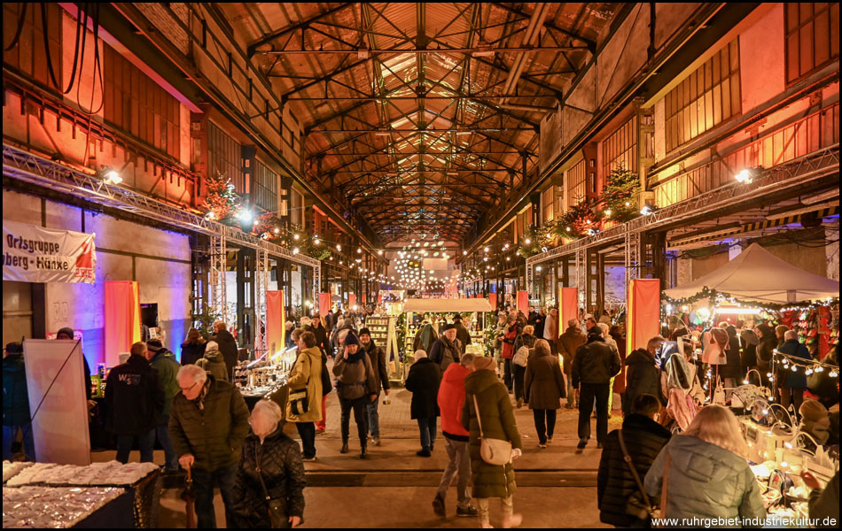 Zentralperspektive mit Blick in eine lange halle mit farbiger Beleuchtung und Weihnachtsmarkt-Ständen