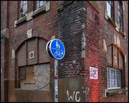 Ecke einer Ziegelstein-Halle, die beleuchtet wird von roten Scheinwerfern. Davor ein blaues Radweg-Schild