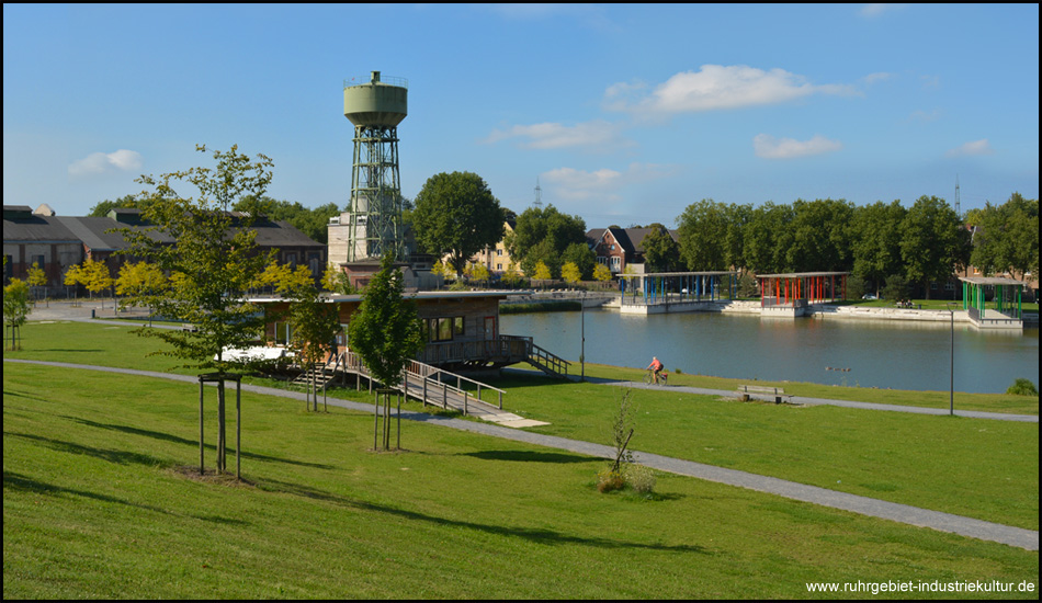 Bergpark Lohberg mit Blick aus erhöhter Lage auf einen Teich und den Wasserturm des Bergwerks dahinter.