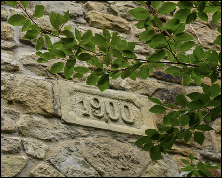 Mauer mit Jahreszahl 1900 und ein Ast eines Baumes