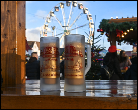 Zwei Tassen mit "Cranger Weihnachtszauber" stehen auf einem Tisch. Im Hintergrund ein Riesenrad