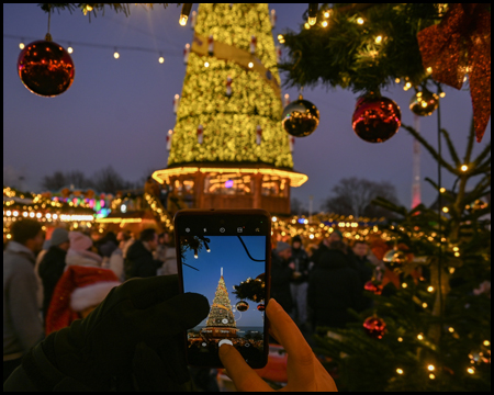 Eine Person fotografiert mit dem Smartphone einen leuchtenden Weihnachtsbaum