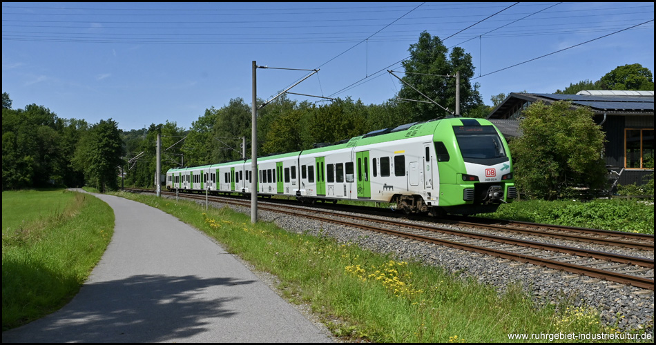 Ein grün-weißer Elektro-Triebwagen als Zug auf einer Eisenbahnstrecke neben einem Radweg