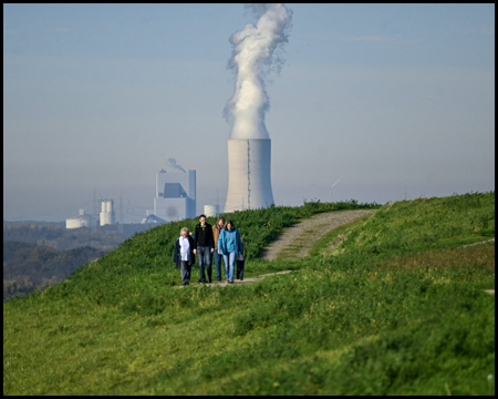 Spaziergänger auf einem Berg vor einem Kühlturm mit Dampfwolken