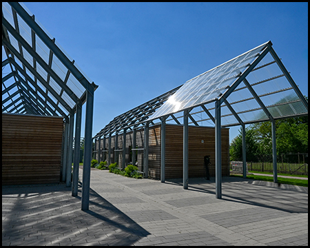 Nahaufnahme der modernen Stahlkonstruktion mit Glasdach und Holzwänden unter klarem Himmel.