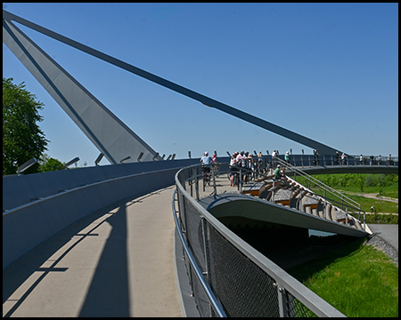 Eine moderne Brücke mit markanter Stahlkonstruktion, auf der Besucher entlanglaufen und die grüne Landschaft bewundern.