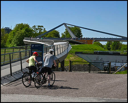Zwei Radfahrer betrachten die Aussicht von einer Aussichtsplattform neben einer modernen Brückenkonstruktion.