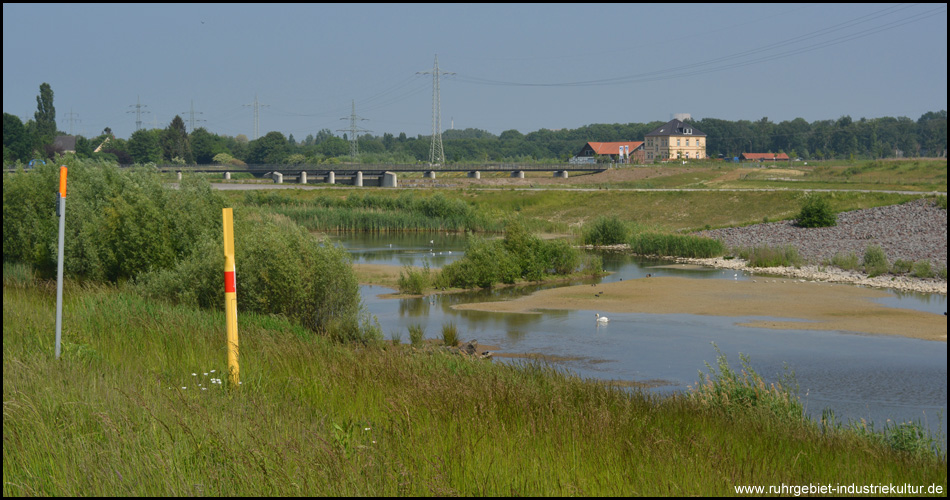 Nebenarm des Rückhaltebeckens. Dahinter Brücke auf dem Damm und Rückstauwehr und rechts der Hof Emschertal