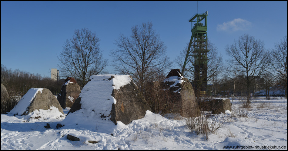 Betonfundamente und Förderturm mit Fußspuren im Schnee