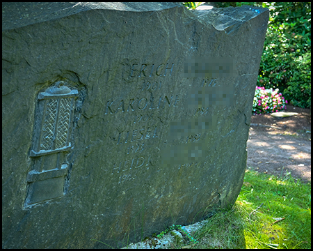 Verwitterter, historischer Grabstein mit kaum noch lesbaren Inschriften und einem Symbol einer Grubenlampe aus dem Bergbau.