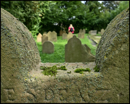Blick durch runde Oberseiten eines Grabsteines auf einen Friedhof