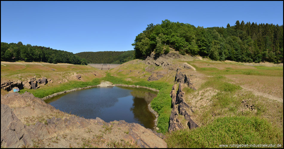 Restsee inmitten der Felsen, hinten ist die Staumauer zu sehen