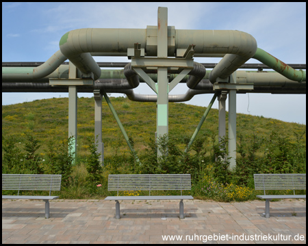 Sitzbänke vor Rohrleitungen und dem Aussichtshügel