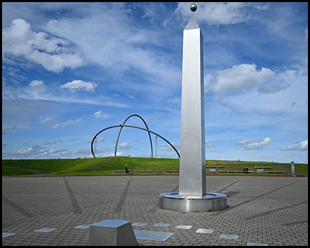 Obelisk im Vordergrund mit der Stahlbögen des Horizontobservatoriums auf dem grünen Hügel im Hintergrund.