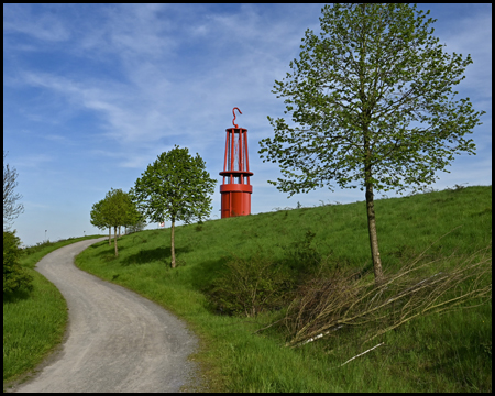 Ein Weg schlängelt sich einen Hang hinauf zu der roten großen Grubenlampe der Halde Rheinpreußen.