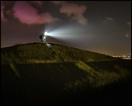 Ein einzelner Hügel bei Nacht mit einem starken Scheinwerfer, der einen hellen Lichtstrahl in den Nachthimmel wirft.