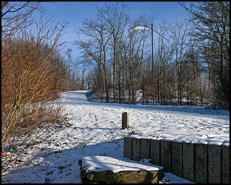 Verschneite Wege auf einer Halde, im Hintergrund ist der Windzeiger durch das kahle Buschwerk zu sehen