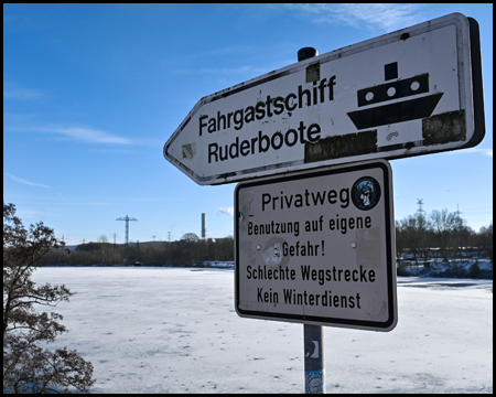 Vereister See und Schild zum Fahrgastschiff und Ruderbootverleih