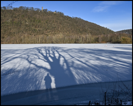 Seefläche mit Eis und Schatten von Bäumen und einer Person darauf