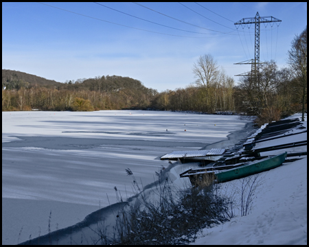 Zugefrorener See mit Booten am Ufer im Schnee