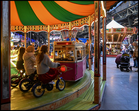 Kinderkarussell mit Fahrrädern und einer Straßenbahn, hinten ein Kettenkarussell