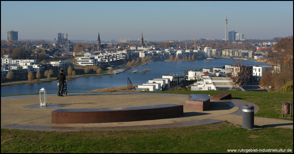 Aussicht vom Landschaftsbauwerk Kaiserberg II auf den PHOENIX See, hinten Florianturm, Westfalenstadion, Telekom-Hochhaus. Verdeckt hinter den Neubauten am Hafen die Hörder Burg. Rechts neue Wohnbebauung, davor Fuß- und Radweg um den See. 