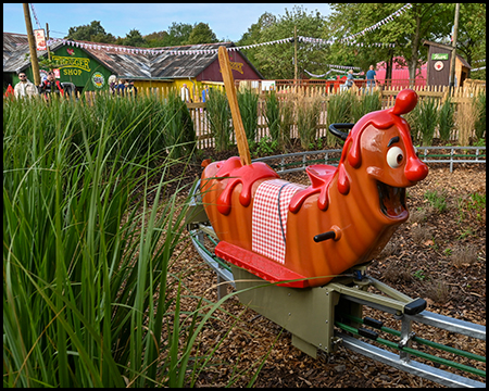 Fahrgeschäft Einschienenbahn mit einer fahrenden Currywurst, die man reiten kann. Die Anlage führt durch hohe, grüne Gräser.