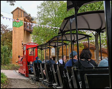 Eine Parkeisenbahn mit roter Lok fährt auf einen Turm mit der Beschriftung Karls Erlebnis-Dorf zu.