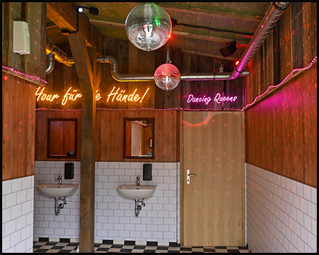 Waschraum einer Toilette mit Disco-Kugel, Leuchtbändern und Leuchtschrift "Dancing Queen"