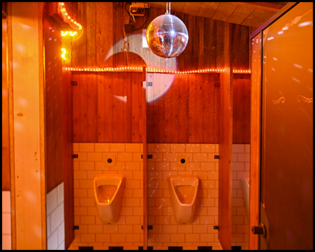 Urinale einer Herrentoilette mit Disco-Kugel und LED-Bändern