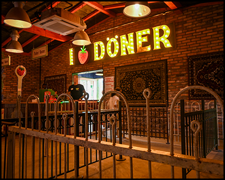 Innenaufnahme eines Gebäudes mit Teppichen an der Wand, darüber der Text I love Döner, wobei das Herz eine Erdbeere darstellt.