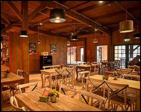 Tische und Stühle eines Restaurants. Die Lampen unter der Decke bestehen aus umgedrehten Kochtöpfen.