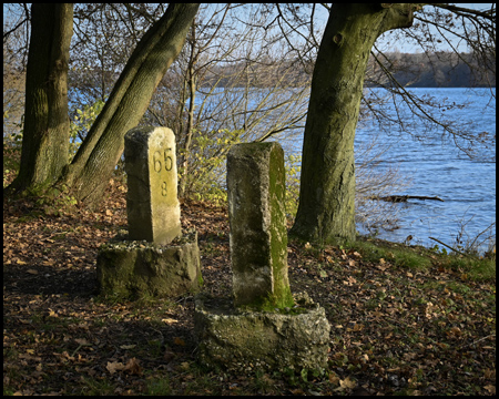 Steine mit Kilometerangaben am Ufer eines Sees