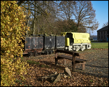 Grubenlok und Loren als Denkmal auf einer Wiese mit Herbstlaub