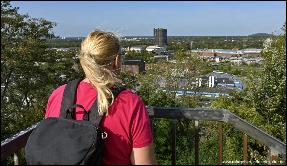 Eine Frau steht an einem Geländer und schaut auf die Gebäude und den Gasometer der Neuen Mitte Oberhausen