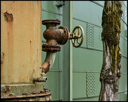 Handrad an einem Rohr vor einem grünen Stahlgebäude