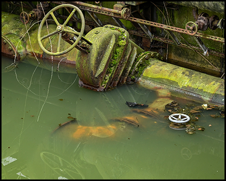 Unter Wasser stehende rohre und Handregler. Das Wasser ist trüb und grün.