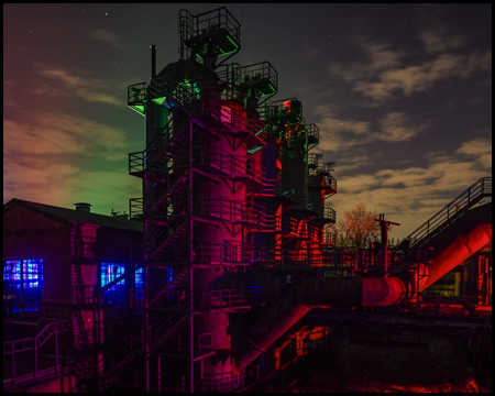 Lila beleuchtete Silos einer Industrieanlage mit Scheinwerferschein, der wirkt wie Nordlicht am Himmel