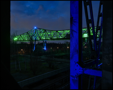 Blau beleuchtete Stahlträger vor dem grün beleuchteten Krokodil, einem Krank im Landschaftspark Duisburg-Nord