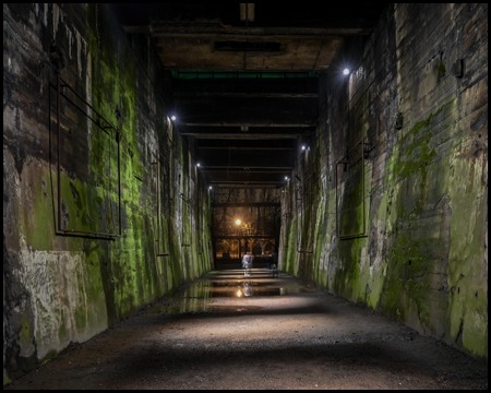 Ein Tunnel mit maroden Betonwänden und mit Moos in der Dunkelheit, nur durch Laternen beleuchtet