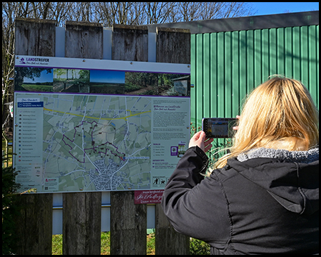 Eine Person fotografiert eine große Übersichtskarte an einer Informationstafel, die Wanderwege und Sehenswürdigkeiten der Region zeigt.