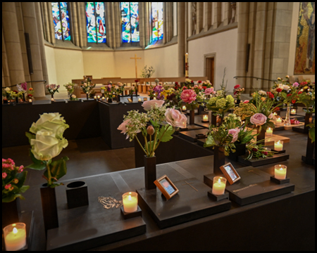 Urnengrabstätten in einer Kirche mit Kerzen und Blumensträußen