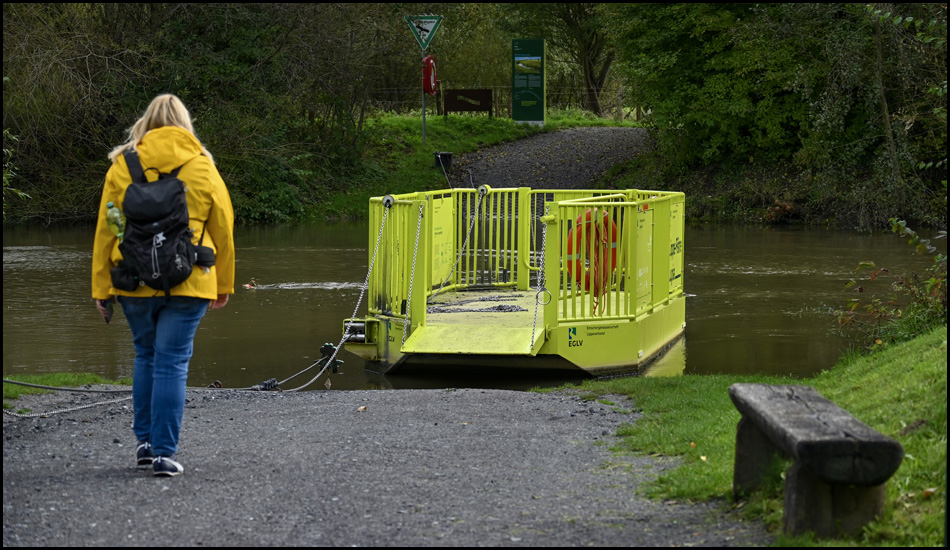 Eine Frau geht auf einen Fluss zu. Dort liegt eine kleine Fähream Ufer.