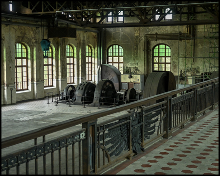 Blick von einer Empore auf eine Halle mit Maschinenteilen. Am Geländer hängt ein hölzerner Wappen-Adler