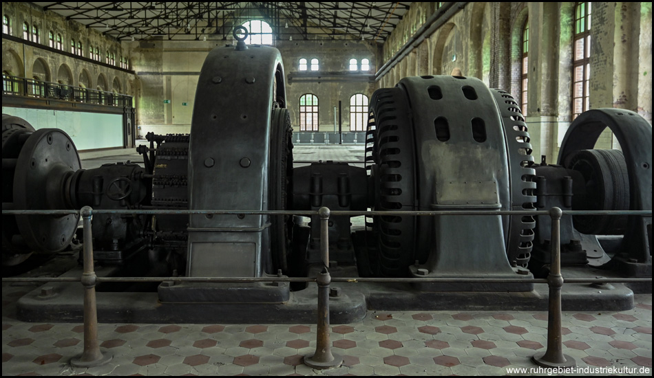 Große Maschinen von der Seite gesehen, dahinter weite Fläche einer sonst leeren Industriehalle