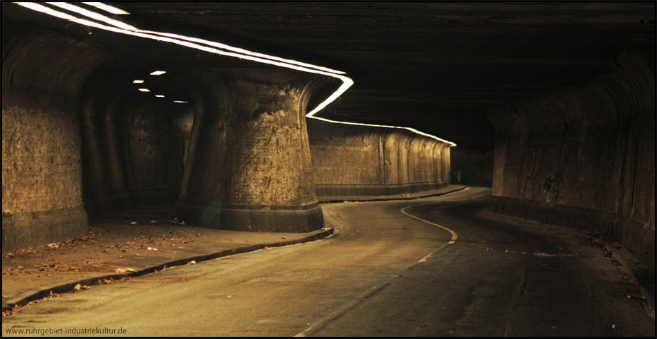 Kurvenreiche Straße mit sichtbaren Schienenresten, links der teilseparierte Fußgängerweg